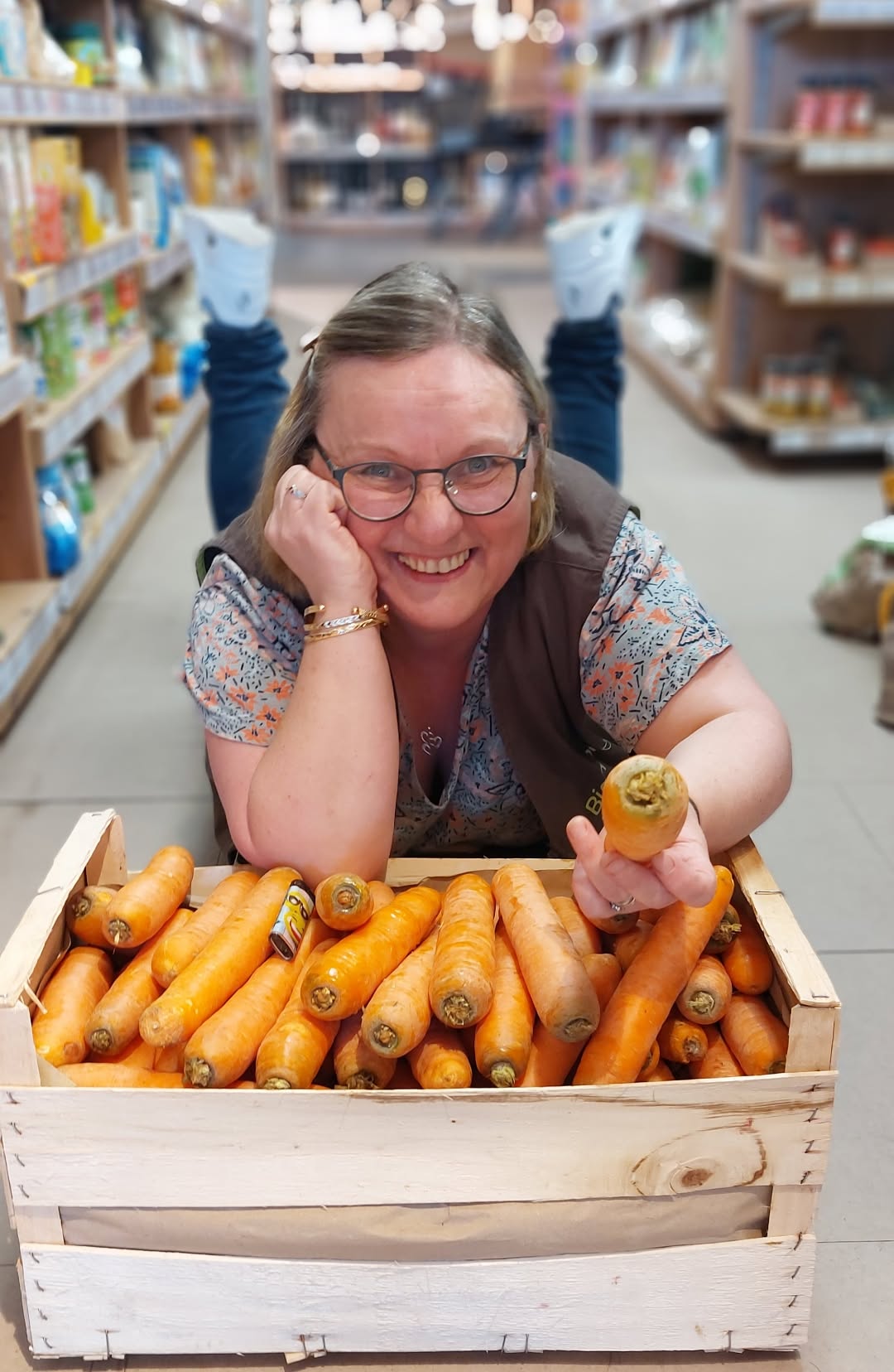Une vendeuse de l'équipe Les Pieds Sur Terre, tout sourire avec une caisse de carottes